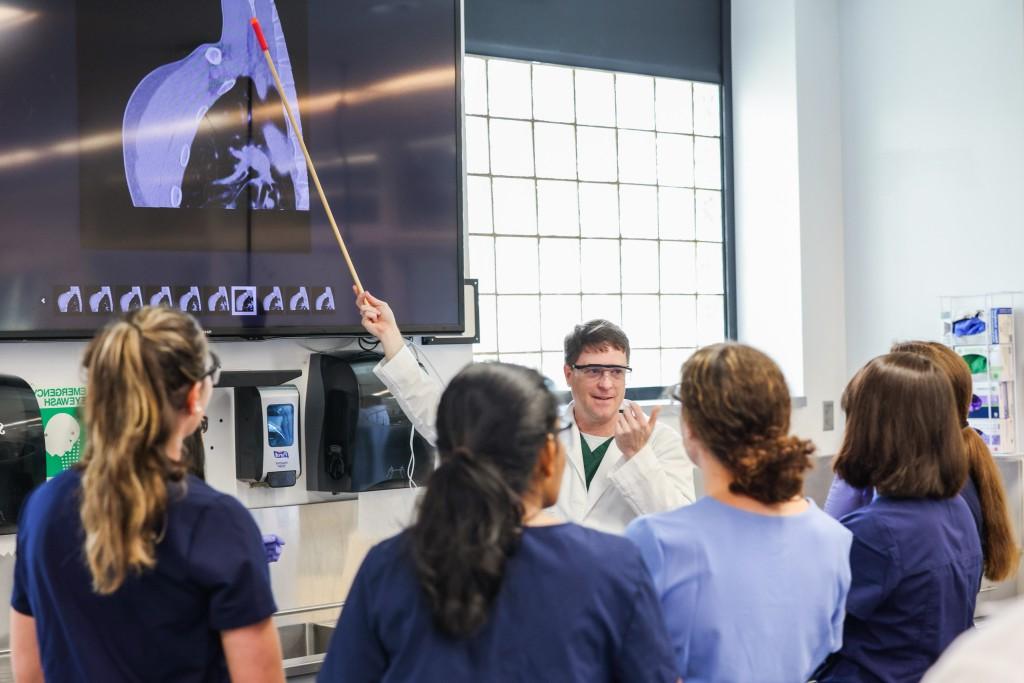 A professor points to a screen as he describes the visuals to a group of anatomy students